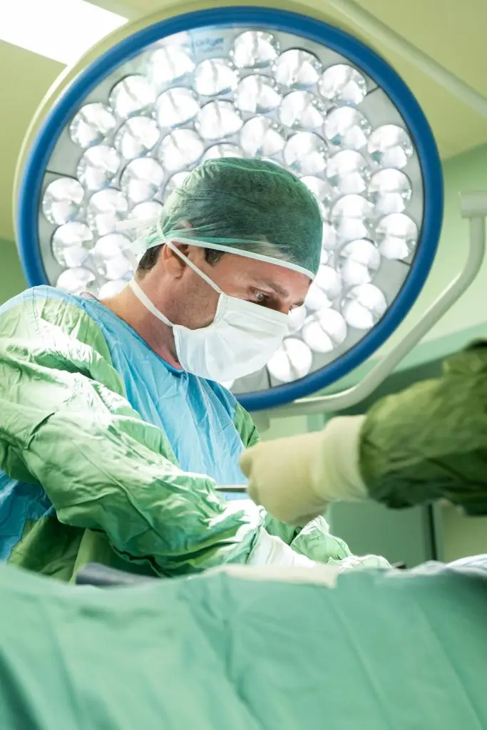 A surgeon in protective gear concentrating while performing a surgical procedure under bright lights.